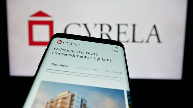 Mão segurando um smartphone que exibe um gráfico de barras financeiro em neon, com fundo tecnológico desfocado, ilustrando a análise das ações cyre3.