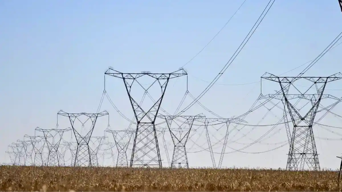 Vista de múltiplas torres de transmissão de energia (linhas de alta tensão) em fila, representando o setor elétrico.