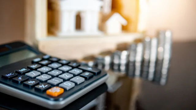 Close-up de uma calculadora preta em foco com pilhas de moedas desfocadas ao fundo, simbolizando o impacto do Relatório de Política Monetária (RPM) do Banco Central na economia.