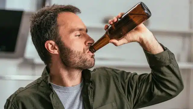 Homem de perfil bebendo cerveja diretamente da garrafa, representando o consumo e a análise de ambev produção fraca.