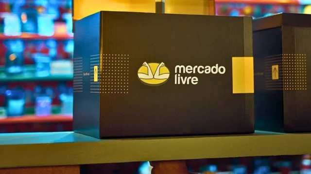 Close-up de uma caixa de papelão preta com o logotipo amarelo do Mercado Livre (aperto de mãos), posicionada em uma prateleira, ilustrando a força logística e o investimento em Mercado Livre ações.