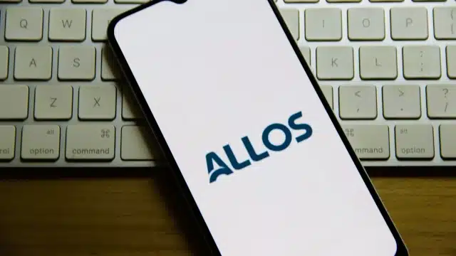 Logo da Allos em tela de celular tendo um teclado ao fundo