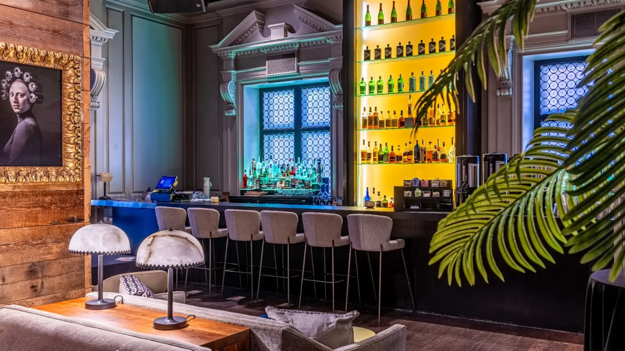 Bar sofisticado com balcão iluminado, prateleiras repletas de garrafas, banquetas estofadas e decoração elegante em ambiente intimista.