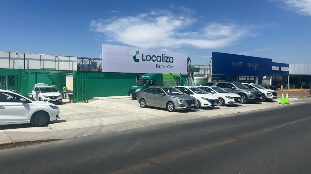 Agência e pátio da Localiza Rent a Car com frota de veículos estacionados sob céu azul.