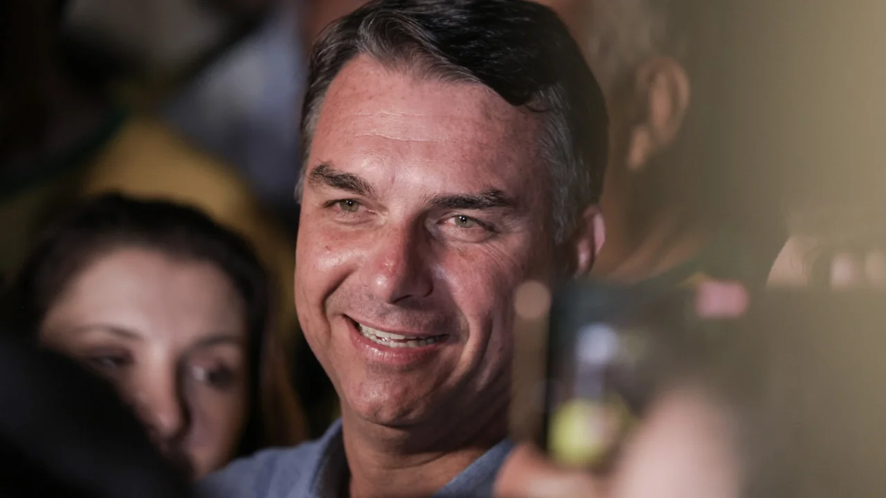 O senador Flávio Bolsonaro sorri cercado por apoiadores em evento político em Brasília.