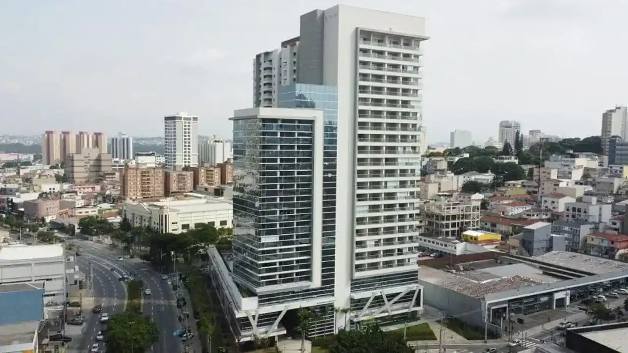 Vista aérea do empreendimento Helbor Patteo Bosque Maia em Guarulhos (SP), composto por edifício residencial e comercial moderno com fachadas claras e espelhadas, localizado ao lado de avenidas e do centro urbano de Guarulhos.