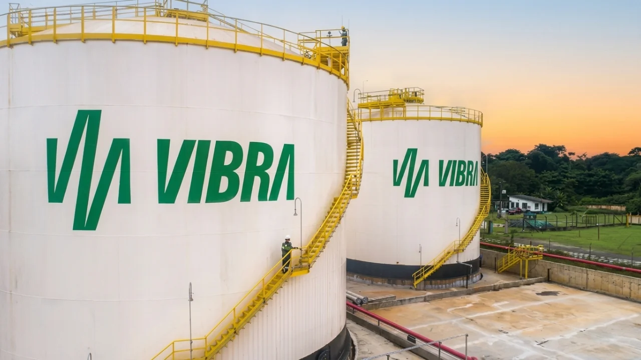 Dois tanques gigantes de armazenamento de combustível de cor branca com o logotipo verde da Vibra Energia, com escadas amarelas e um operador ao lado, em base operacional ao entardecer.